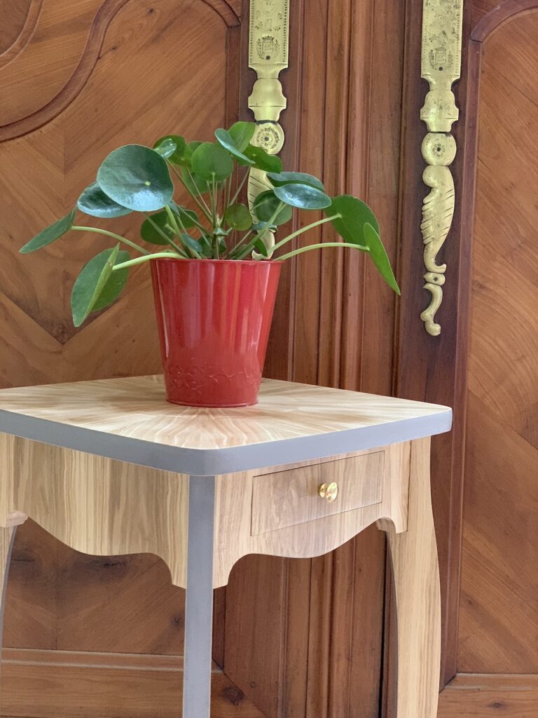 petite sellette en bois, avec des formes galbées et chantournées, surmontée d'un pot de fleur en métal rouge. 